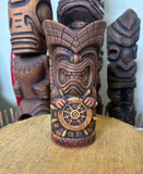 front view of a slipcase brown ceramic tiki mug with a detailed face, green leaves, and gold accents.